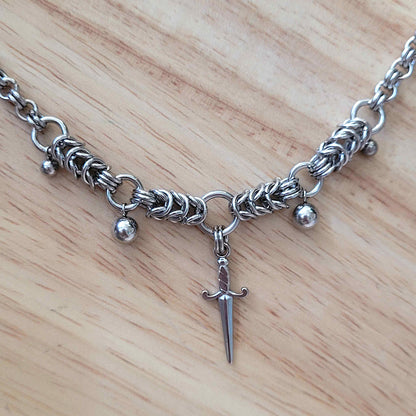 Silver chain necklace with a sword-shaped pendant on a wooden surface