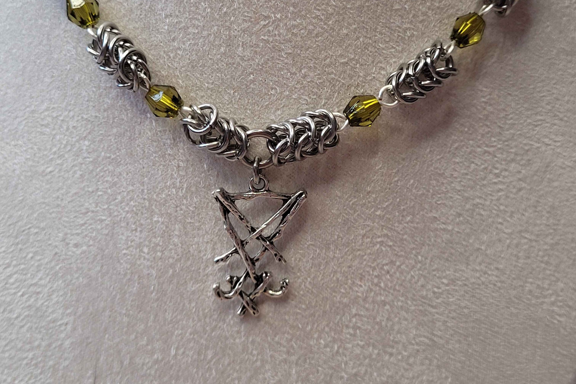 Necklace with silver chain, green beads, and a small silver pendant on a light gray background